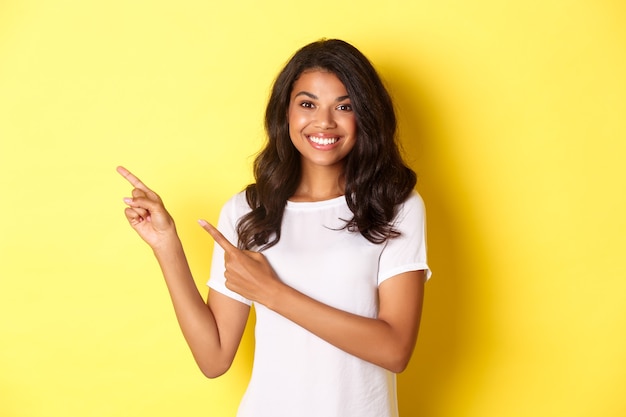Portrait of cheerful and cute african american girl pointing fingers left and smiling showing