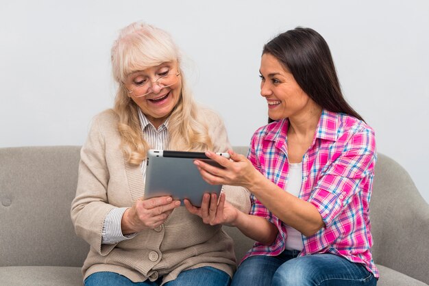 Portrait of cheerful daughter showing digital tablet to her senior mother