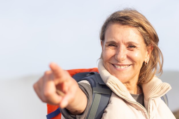 Portrait of cheerful elderly woman with backpack. Sporty woman in casual clothes smiling and pointing. Sport, adventure, hobby concept