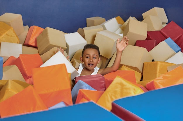 Portrait of cheerful energetic Afro American little boy having fun in trampoline park at weekend