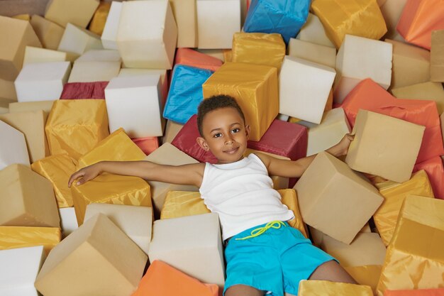 Portrait of cheerful energetic Afro American little boy playing with soft cubes in dry pool