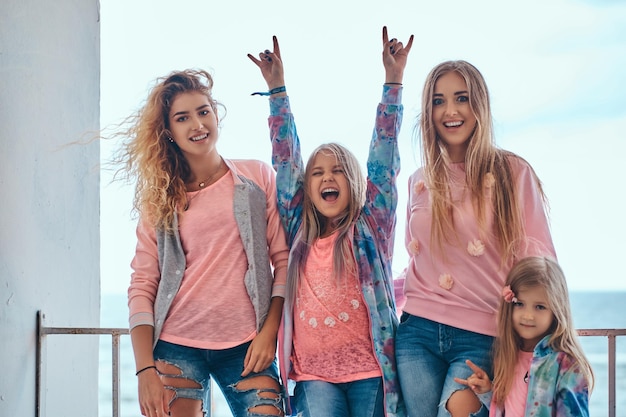Portrait of a cheerful family dressed in trendy clothes posing near a guardrail against a sea coast.