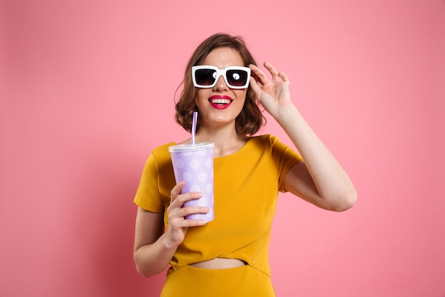 Портрет жизнерадостной девушки в солнечных очках держа чашку
