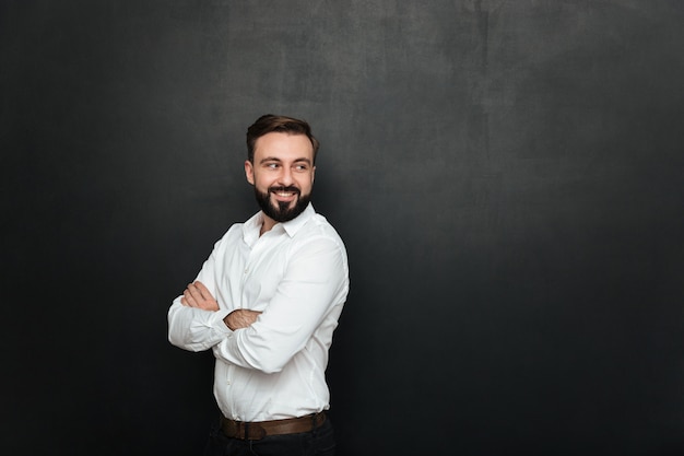 Portrait of cheerful good-looking man standing with arms folded, and looking back over dark gray copy space