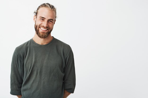 Portrait of cheerful handsome bearded guy with fashionable hairstyle smiling