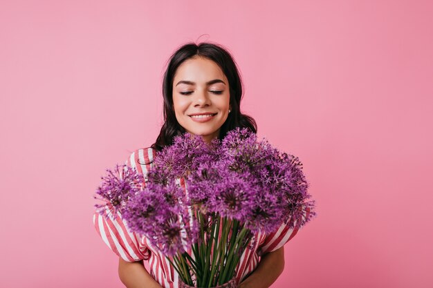 Portrait of cheerful happy girl enjoying smell of flowers. Cute lady with beautiful tan having fun