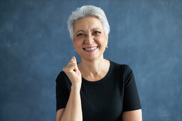 Free photo portrait of cheerful happy middle aged caucasian woman in black t-shirt clenching fist and smiling broadly.