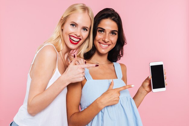 Free photo portrait of cheerful ladies showing blank screen of smartphone isolated