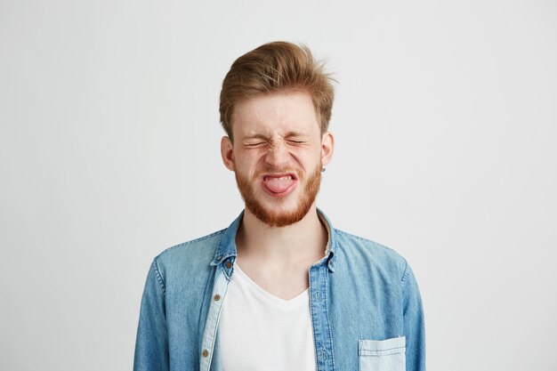 Portrait of cheerful merryyoung man with closed eyes showing tongue.