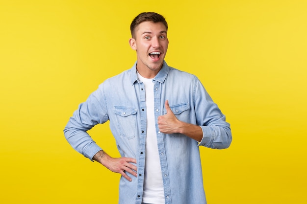 Portrait of cheerful optimistic handsome man encourage people, showing thumb-up in approval. Cute male customer rate good product, agree or like something, standing yellow background satisfied.