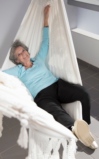 Портрет веселый пенсионерка отдыхает в гамаке на балконе