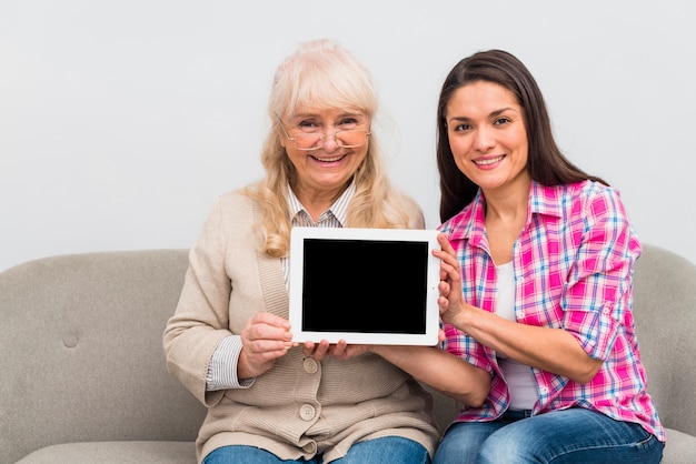 陽気な先輩母と彼女の娘が黒い画面でデジタルタブレットを示すの肖像画