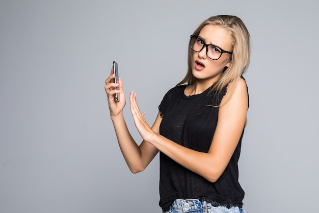 Free photo portrait of a cheerful woman covering microphone on smartphone and looking at camera isolated on gray background