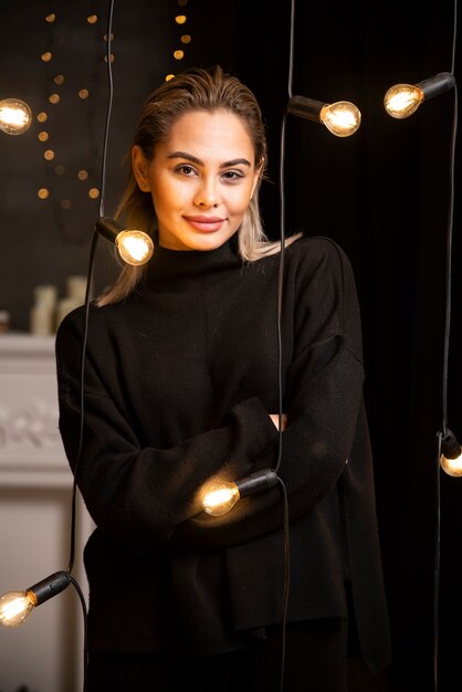 Portrait of a cheerful woman in dark sweater standing near lamps .