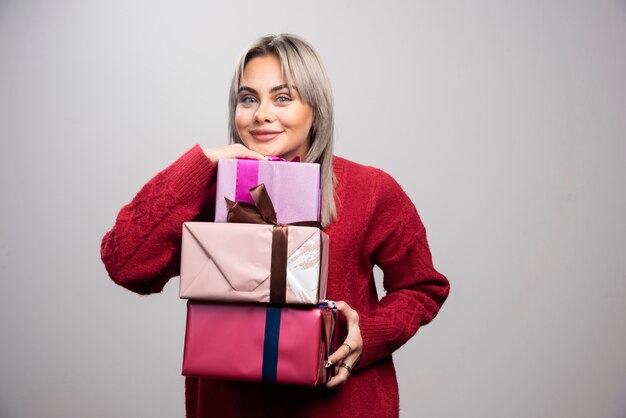 Portrait of cheerful woman holding holiday gifts on gray background.