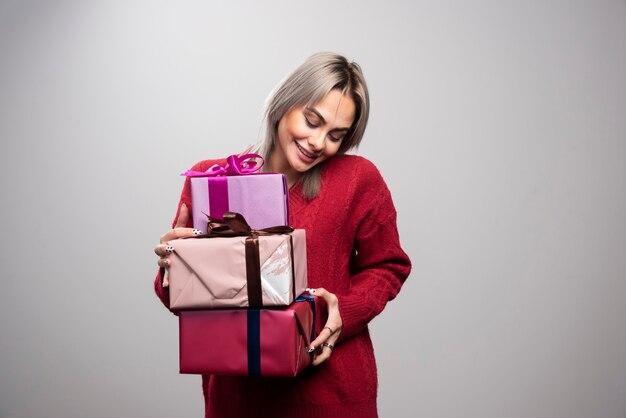 Portrait of cheerful woman holding holiday gifts on gray background.