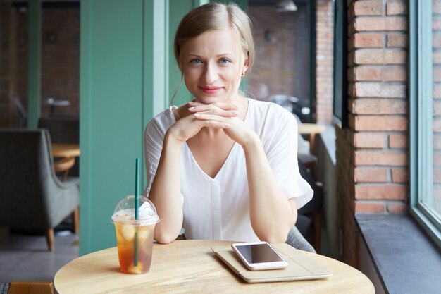 カメラ目線とカフェのテーブルで笑顔の陽気な女性の肖像画