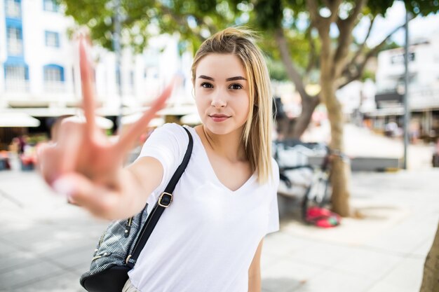 Portrait of a cheerful woman. Lovely woman showing victory or peace sign outdoors in summer street.