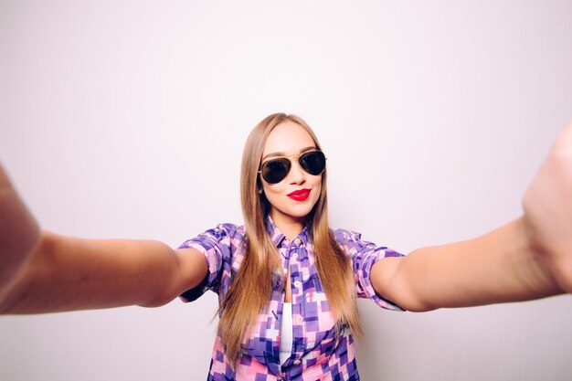 Portrait of a cheerful woman making selfie photo over gray wall