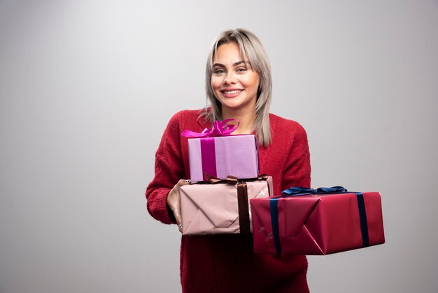 Portrait of cheerful woman offering holiday gifts on gray background.