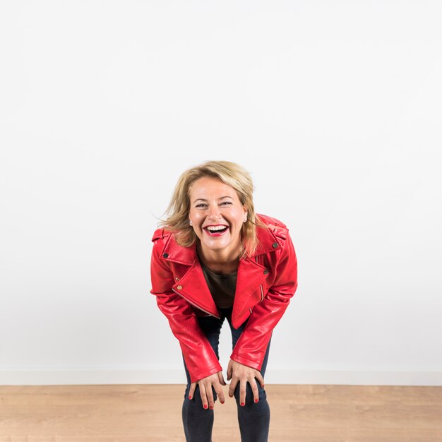 Portrait of cheerful woman in red leather jacket laughing against white wall