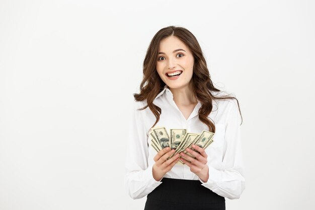 Portrait of a cheerful young business woman holding money banknotes and celebrating isolated over white background