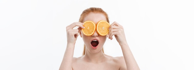 Foto gratuita ritratto di una giovane ragazza allegra che tiene due fette di arancia in faccia sopra il muro bianco backgr
