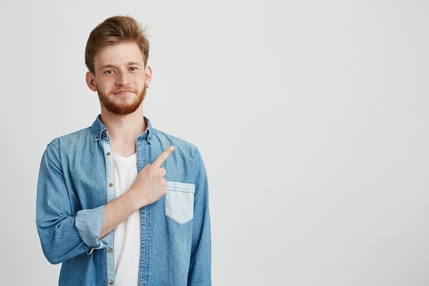 Portrait of cheerful young handsome guy smiling pointing finger up.