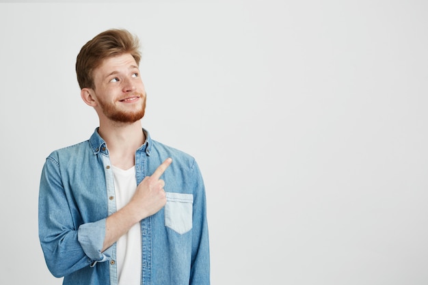 Portrait of cheerful young handsome man smiling pointing finger up