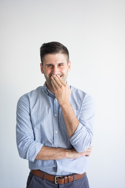 Portrait of cheerful young man covering mouth while laughing.