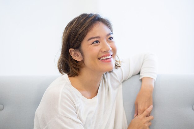 Portrait of cheerful young woman sitting on coach at home