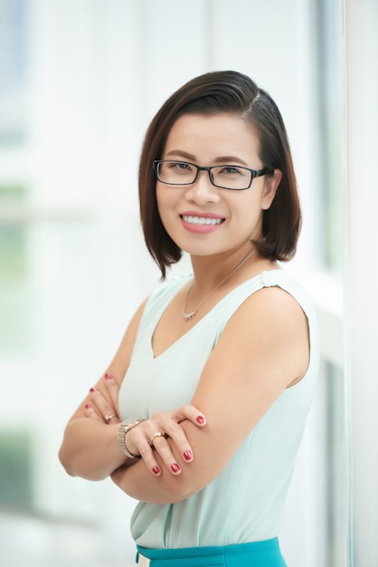 Portrait of cheerful young woman standing with folded arms at the window