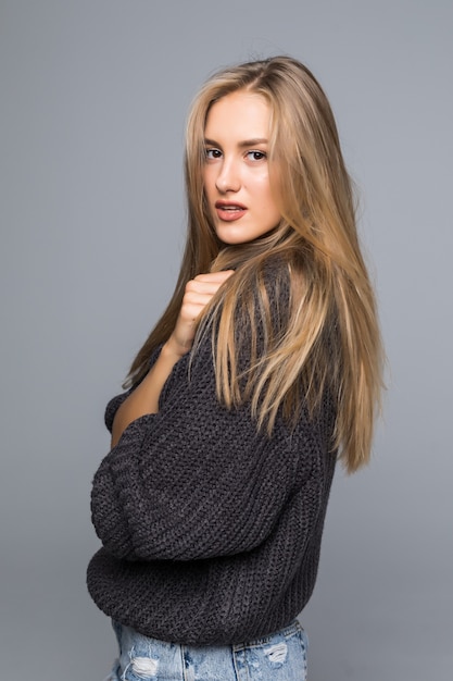 Free photo portrait of a cheerful young woman in sweater smiling with arms crossed on gray background