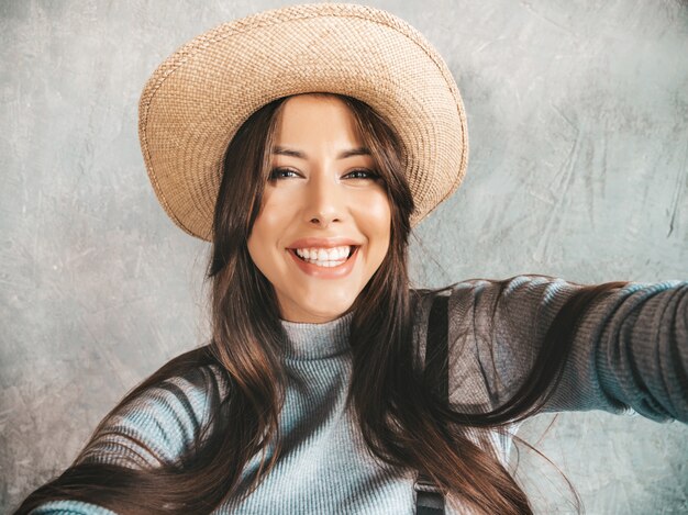 Portrait of cheerful young woman taking photo selfie and wearing modern clothes and hat.  