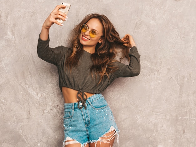 Portrait of cheerful young woman taking photo selfie with inspiration and wearing modern clothes. Girl holding smartphone camera. Model posing