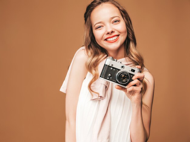 インスピレーションと写真を撮ると白いドレスを着て陽気な若い女性の肖像画。レトロなカメラを保持している女の子。モデルのポーズ