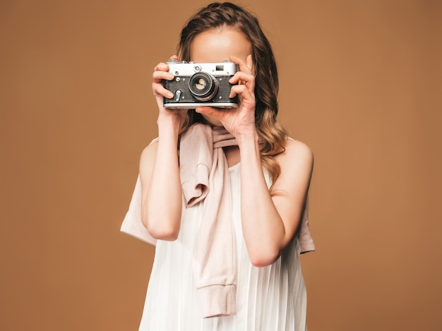 インスピレーションと写真を撮ると白いドレスを着て陽気な若い女性の肖像画。レトロなカメラを保持している女の子。モデルのポーズ