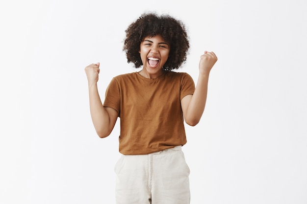 Портрет аплодирующей беззаботной и счастливой торжествующей афро-американской девочки-подростка с афро-прической, поднимающей кулаки в знак победы или победного жеста, широко улыбаясь со звуком да