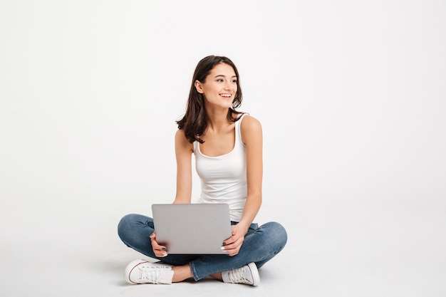 Portrait of a cheery woman dressed in tank-top holding laptop