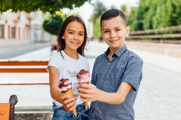 Portrait of children, brother and sister on the bench eating sweet ice cream.