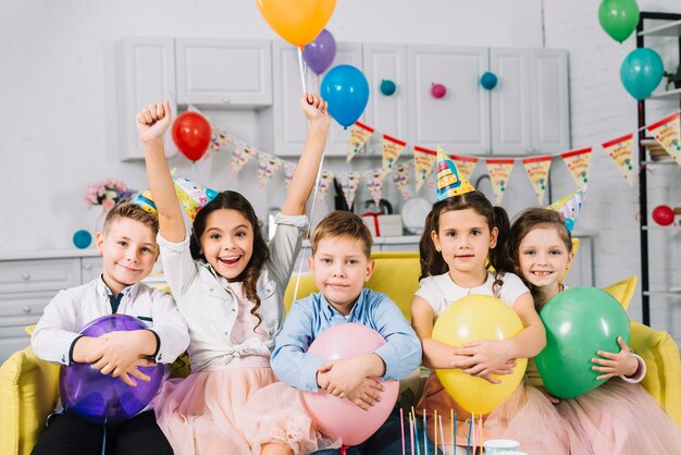 Portrait of children sitting on sofa holding balloons