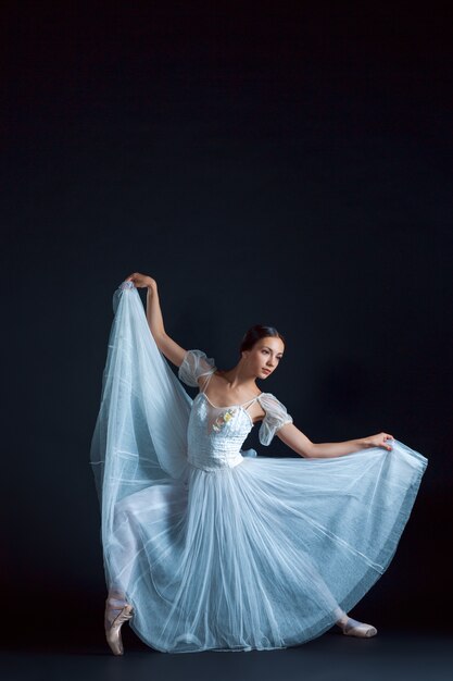 Portrait of the classical ballerina in white dress on black space