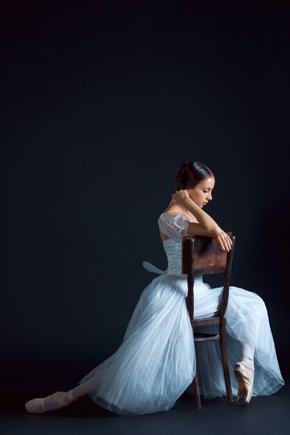 Portrait of the classical ballerina in white dress on black wall