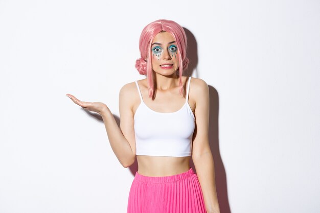 Portrait of clueless cute girl in pink wig shrugging, looking unaware, standing in halloween costume with bright makeup.
