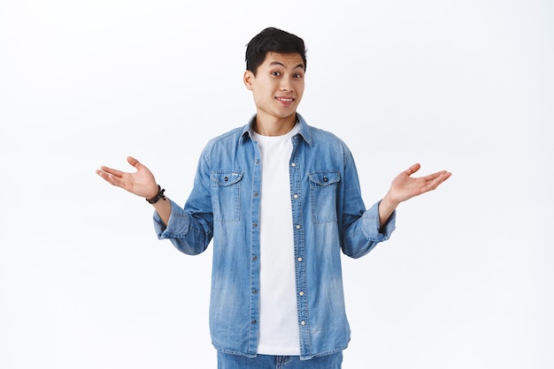 Portrait of clueless handsome asian young man cant answer have no idea shrugging and spread hands sideways unaware acting puzzled as avoiding answering question white background