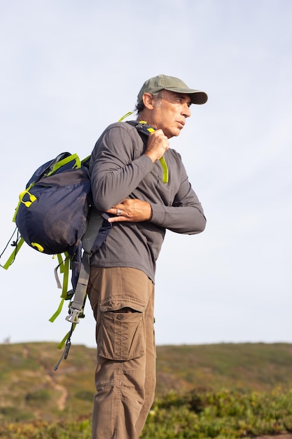 Free photo portrait of concentrated elderly man with backpack. sporty man in casual clothes during hike on summer day. sport, adventure, hobby concept