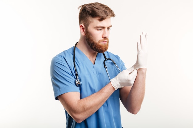Портрет концентрированного молодого доктора надевает стерильные перчатки