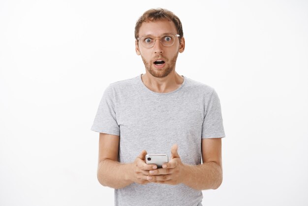 Portrait of concerned shocked mature bearded male gasping opening mouth shocked holding smartphone staring reading strange and disturbing message posing