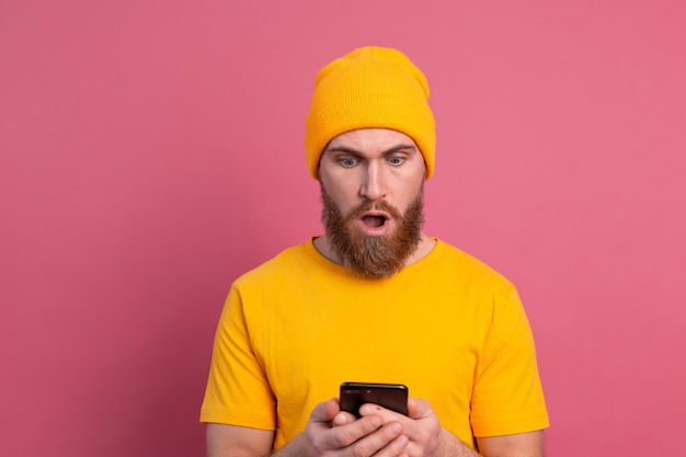 Портрет обеспокоенного шокированного зрелого бородатого мужчины, задыхающегося несчастным, держит смартфон и читает странное и тревожное сообщение на розовом