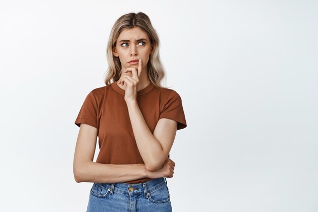 Portrait of concerned woman looking hesitant aside, thinking of something, standing on white